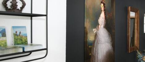A room with a large portrait painting, a wooden shelf with decorative items, and a mirror on the wall.