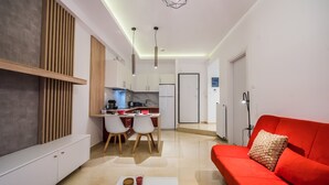 A modern living room with a red sofa, a white coffee table, and a kitchen area with white cabinets and a dining table. - Raspberry Apt by halu! Apartments (Thessaloniki)