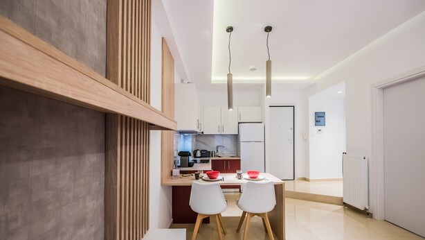 A modern kitchen with a dining area, featuring a wooden accent wall, white chairs, and a countertop with a kettle and coffee maker. - Raspberry Apt by halu! Apartments (Thessaloniki)