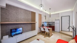 A modern living room with a flat-screen TV, a red sofa, and a dining area with a kitchen in the background. - Raspberry Apt by halu! Apartments (Thessaloniki)