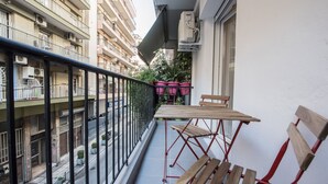 A balcony with a wooden table and chairs, potted plants, and a view of a multi-story building. - Raspberry Apt by halu! Apartments (Thessaloniki)