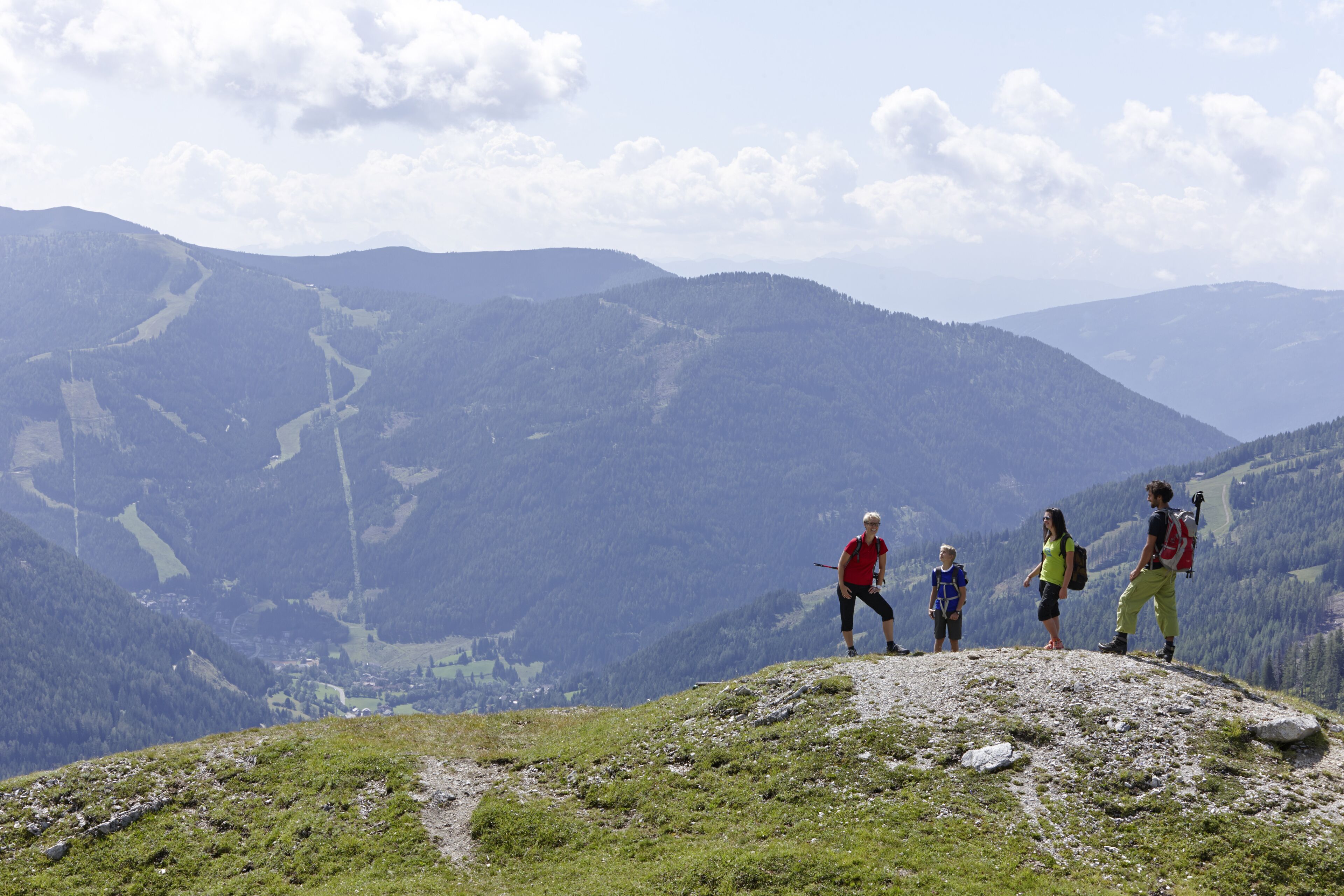 Eine Gruppe Wanderer auf einem Berggipfel mit einem Tal und fernen Bergen im Hintergrund.