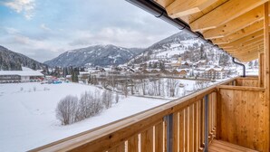 A wooden balcony with a view of a snow-covered village and mountains. - COOEE alpin Hotel Bad Kleinkirchheim (Bad Kleinkirchheim)