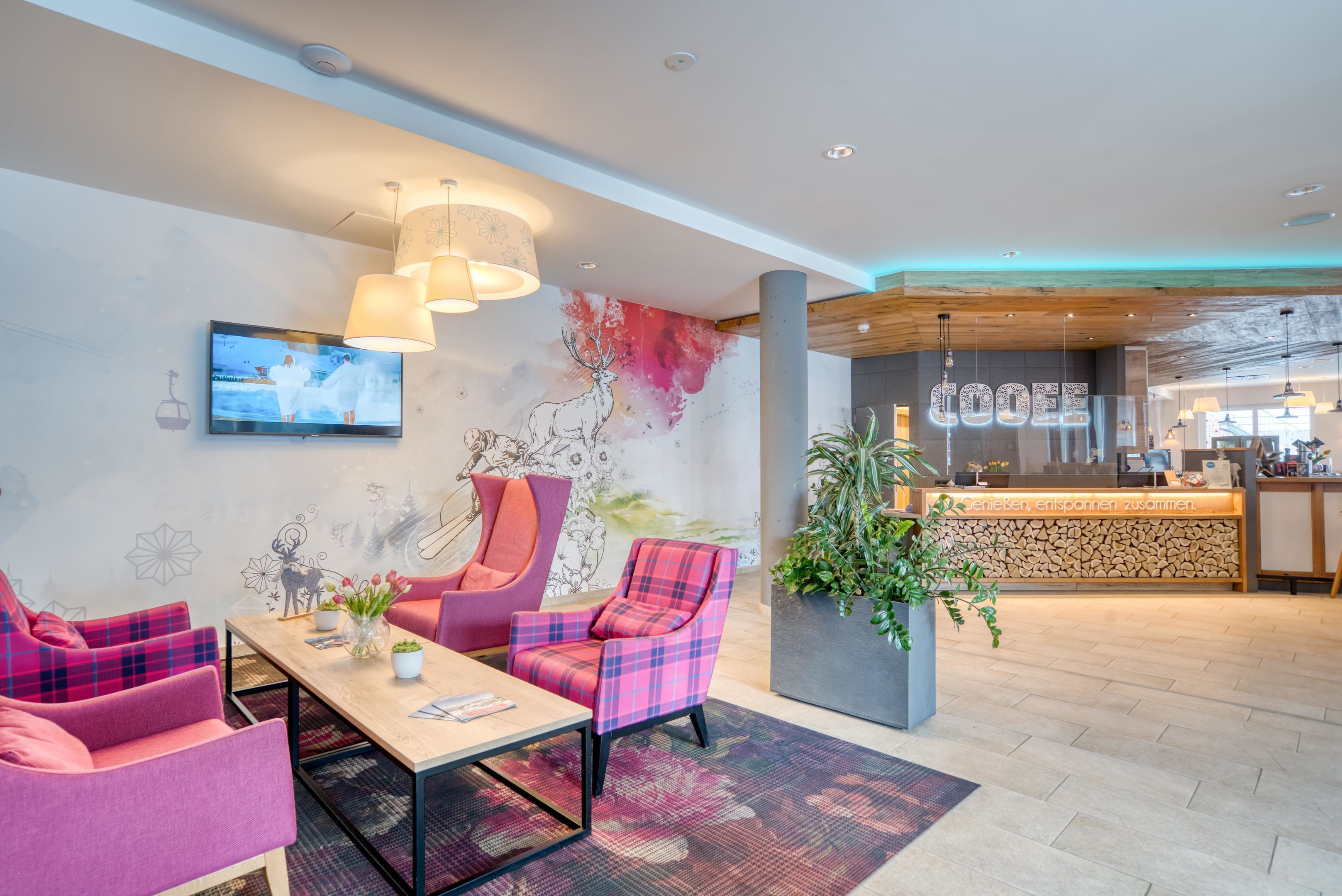 A modern lobby with a reception desk, seating area, and a television displaying a wedding scene.
