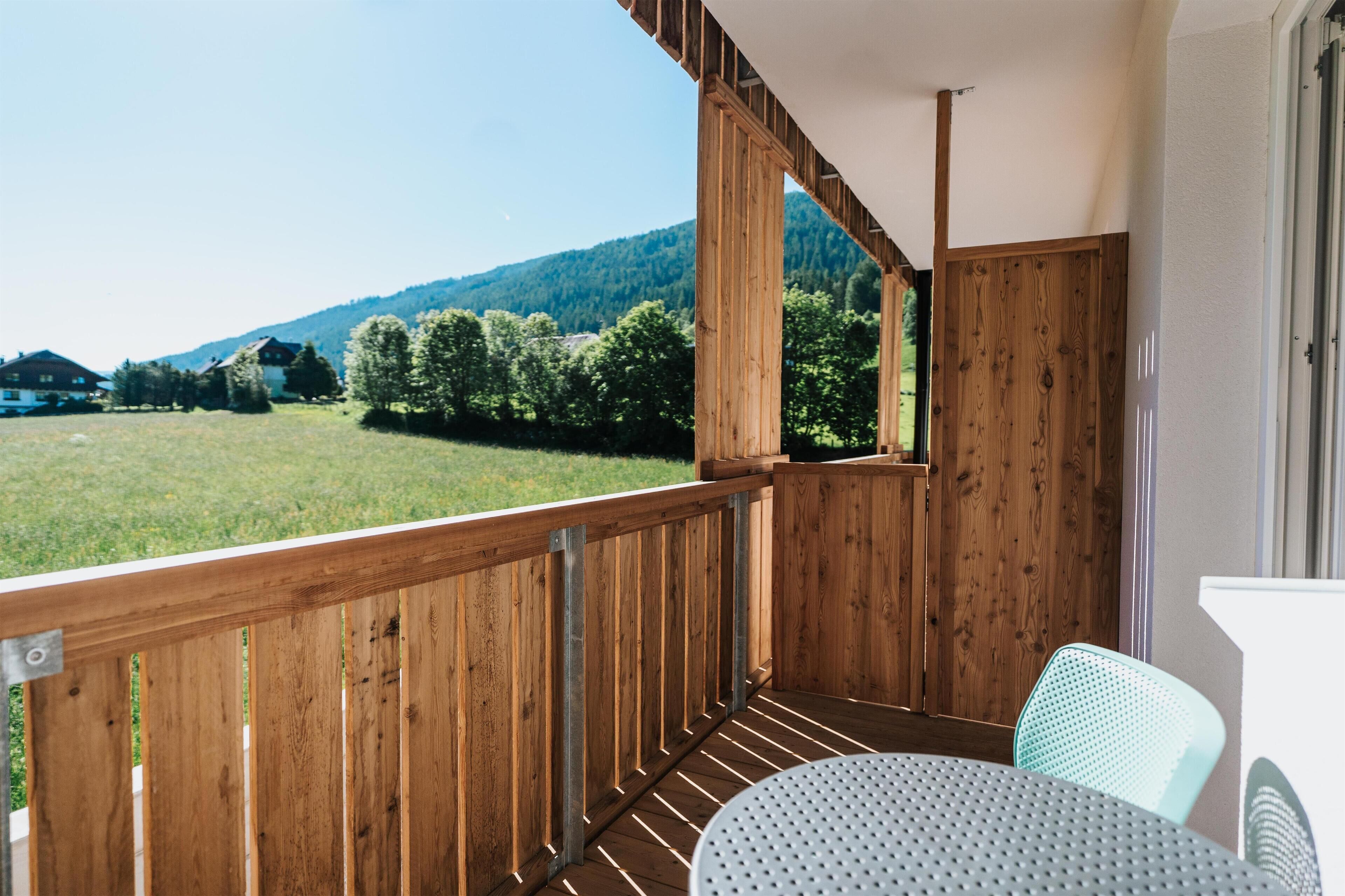 Ein Holzbalkon mit Blick auf ein grünes Feld und Berge.