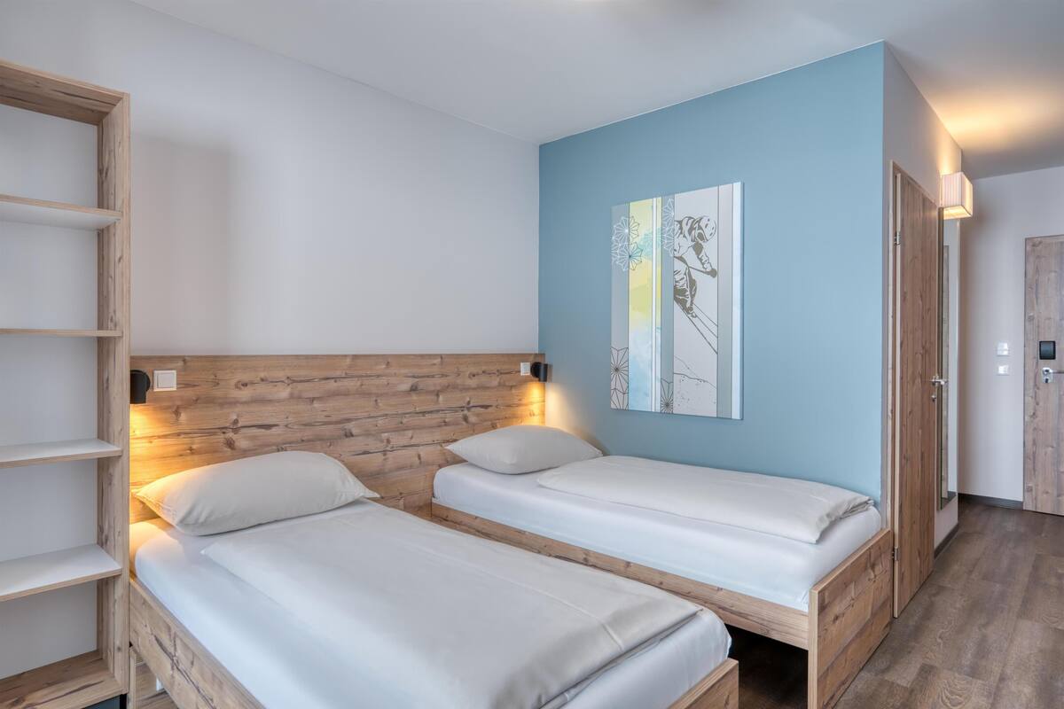 A room with two single beds, wooden headboard, light blue walls, and a wooden wardrobe.