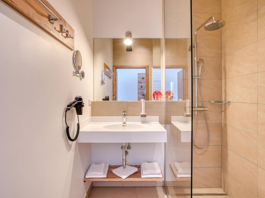 Un baño moderno con cabina de ducha de vidrio, un lavabo blanco y un estante de madera con toallas.