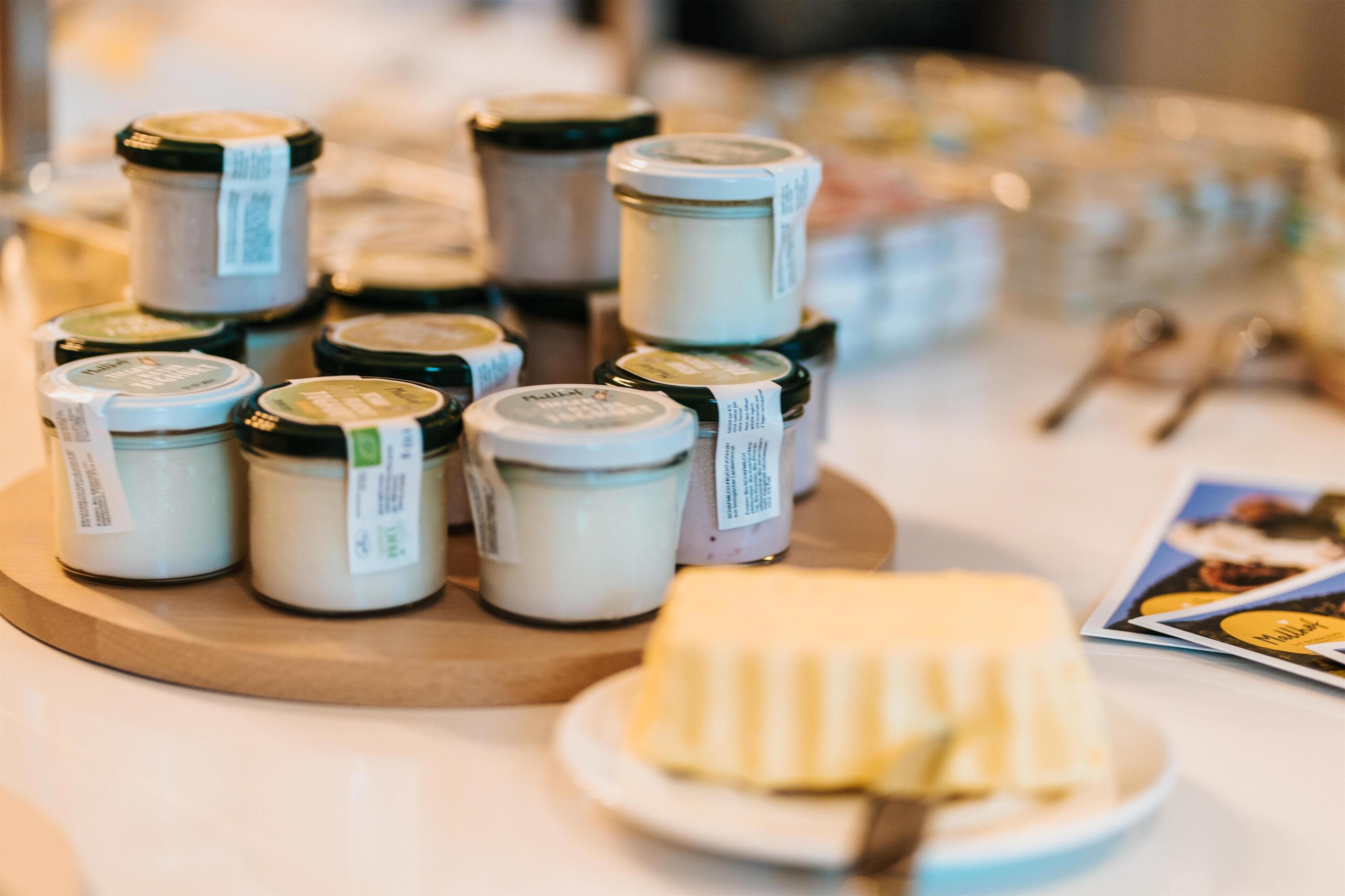 Jars of condiments on a wooden board with a plate of butter.