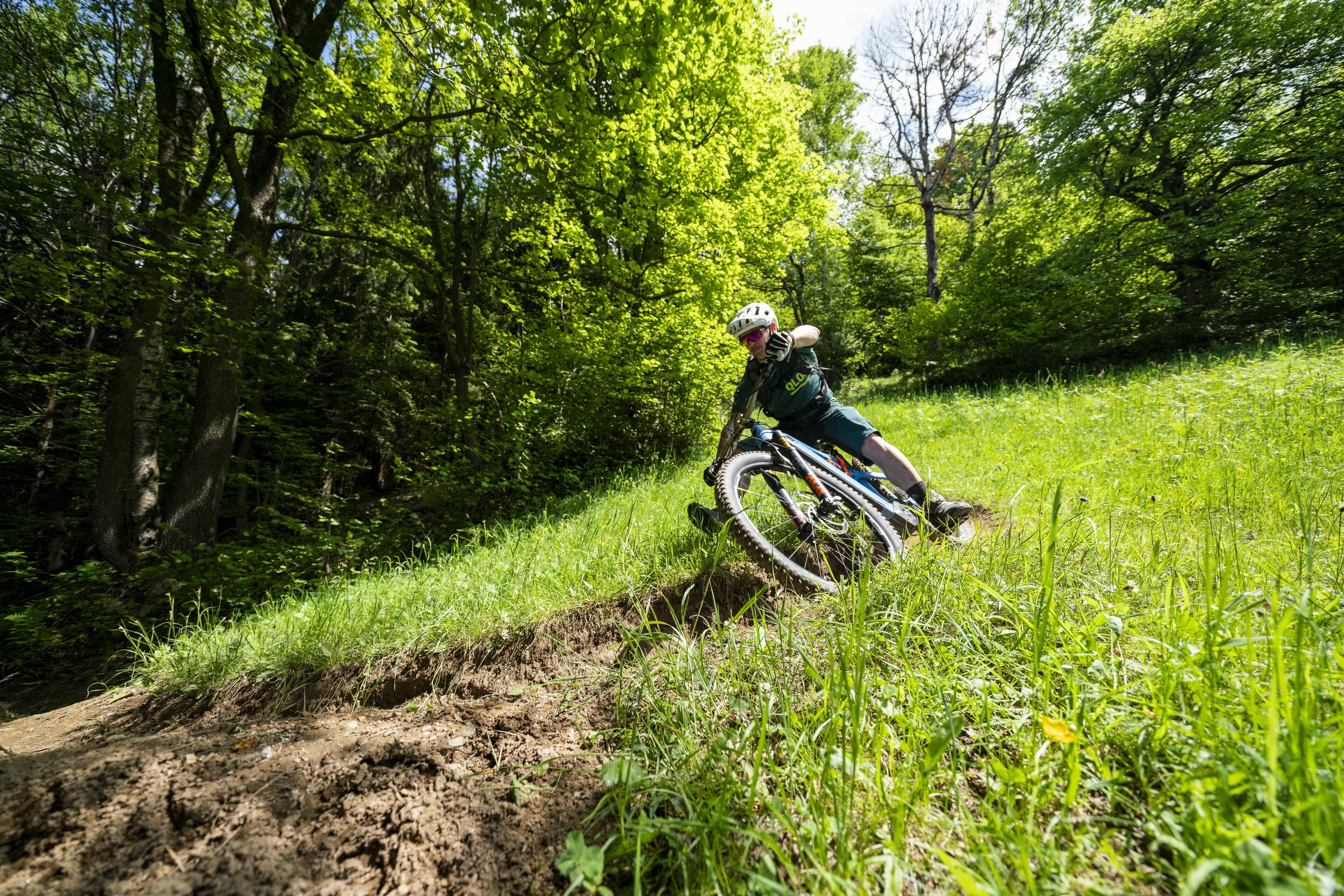 A person riding a mountain bike on a dirt trail surrounded by lush greenery.