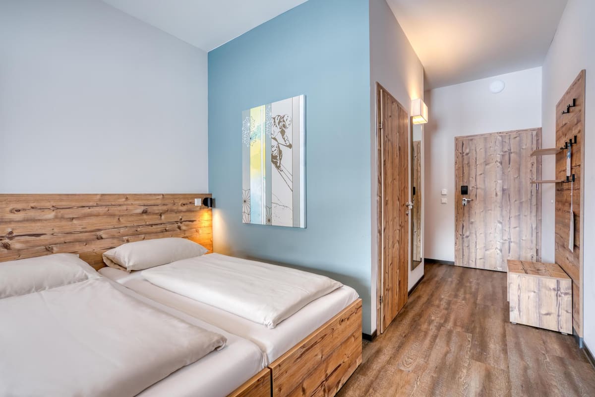A bedroom with two wooden beds, a blue accent wall, and a wooden bench.