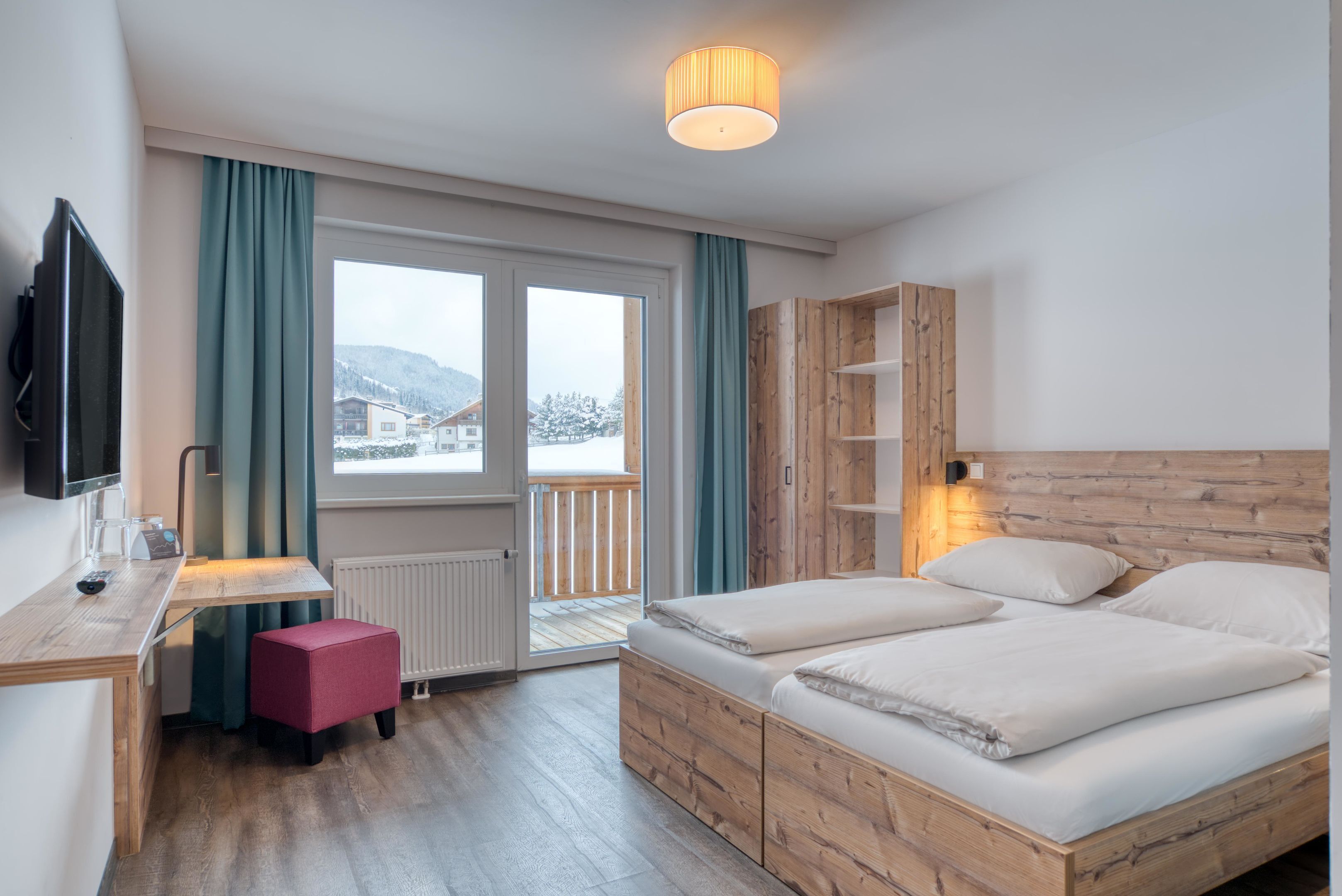A hotel room with a wooden bed, a desk with a chair, a television, and a view of the outside.