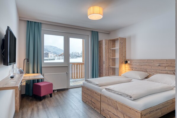 A hotel room with a wooden bed, a desk with a chair, a television, and a view of the outside.