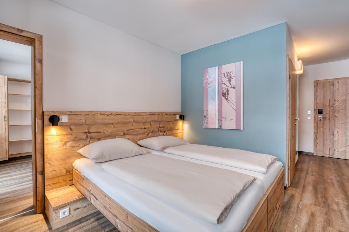 A double bed with a wooden headboard and two bedside lamps, a light blue wall, and a wooden door.