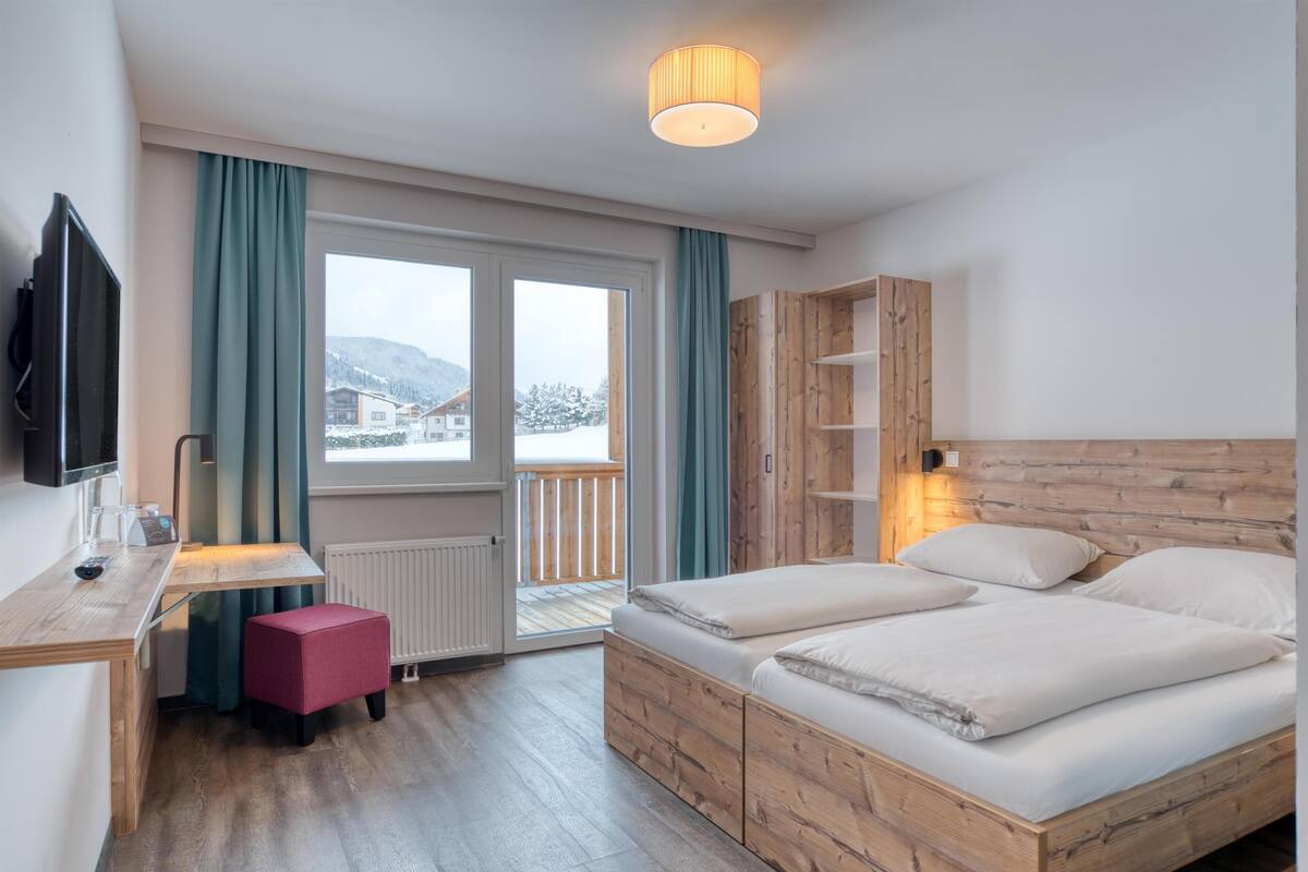 A hotel room with a wooden bed, a desk with a chair, a television, and a window with curtains.