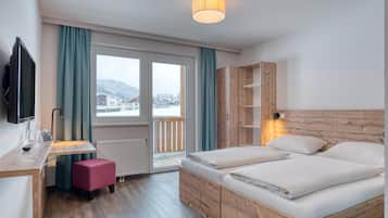 A hotel room with a wooden bed, a desk with a chair, a television, and a window with curtains.