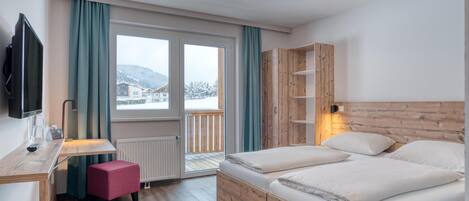Een hotelkamer met een houten bed, een bureau met stoel, een televisie en een raam met gordijnen.
