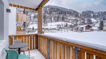 A balcony with a wooden railing overlooking a snow-covered village and mountains.