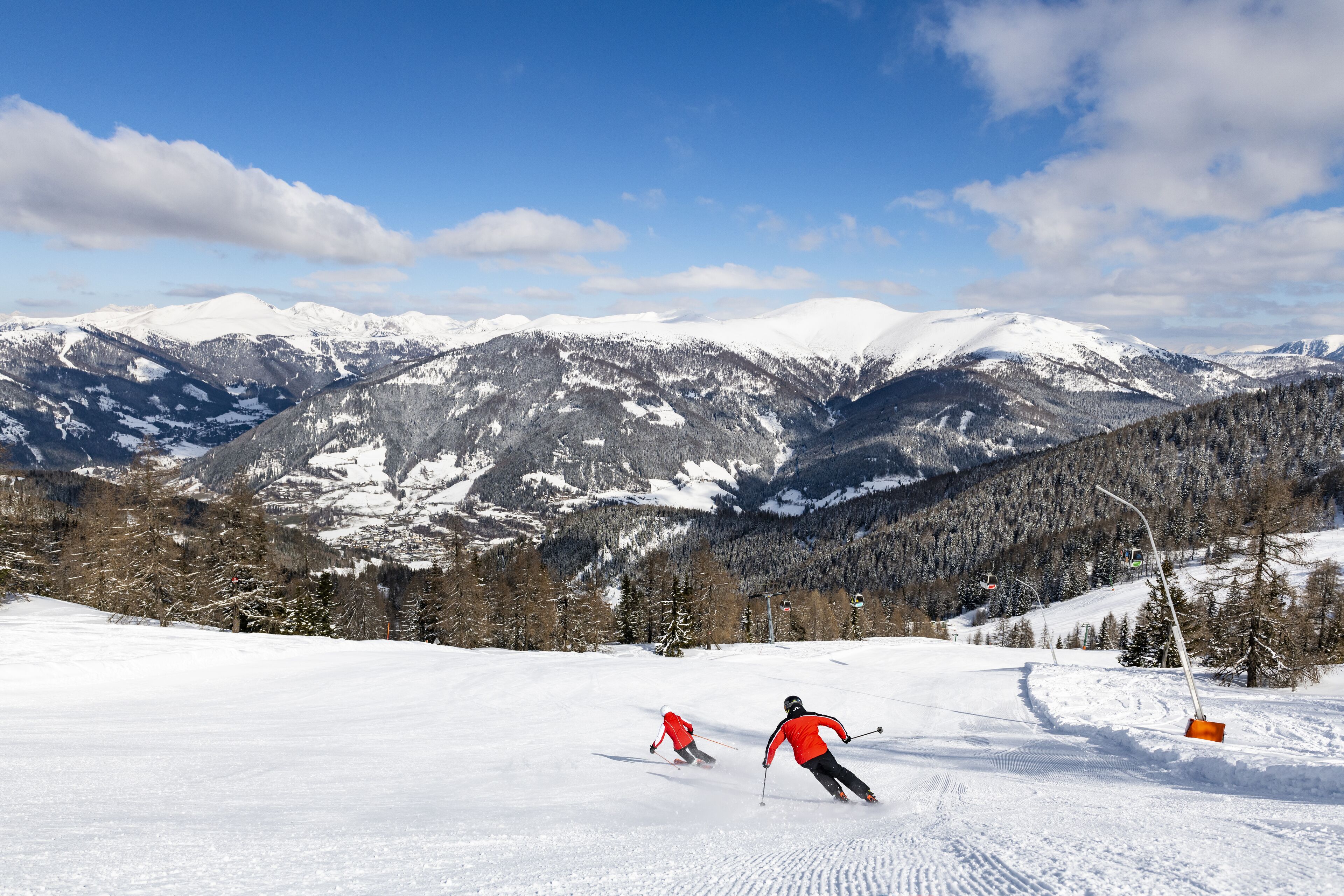 Een besneeuwde skipiste met skiërs, bergen op de achtergrond en een heldere lucht.