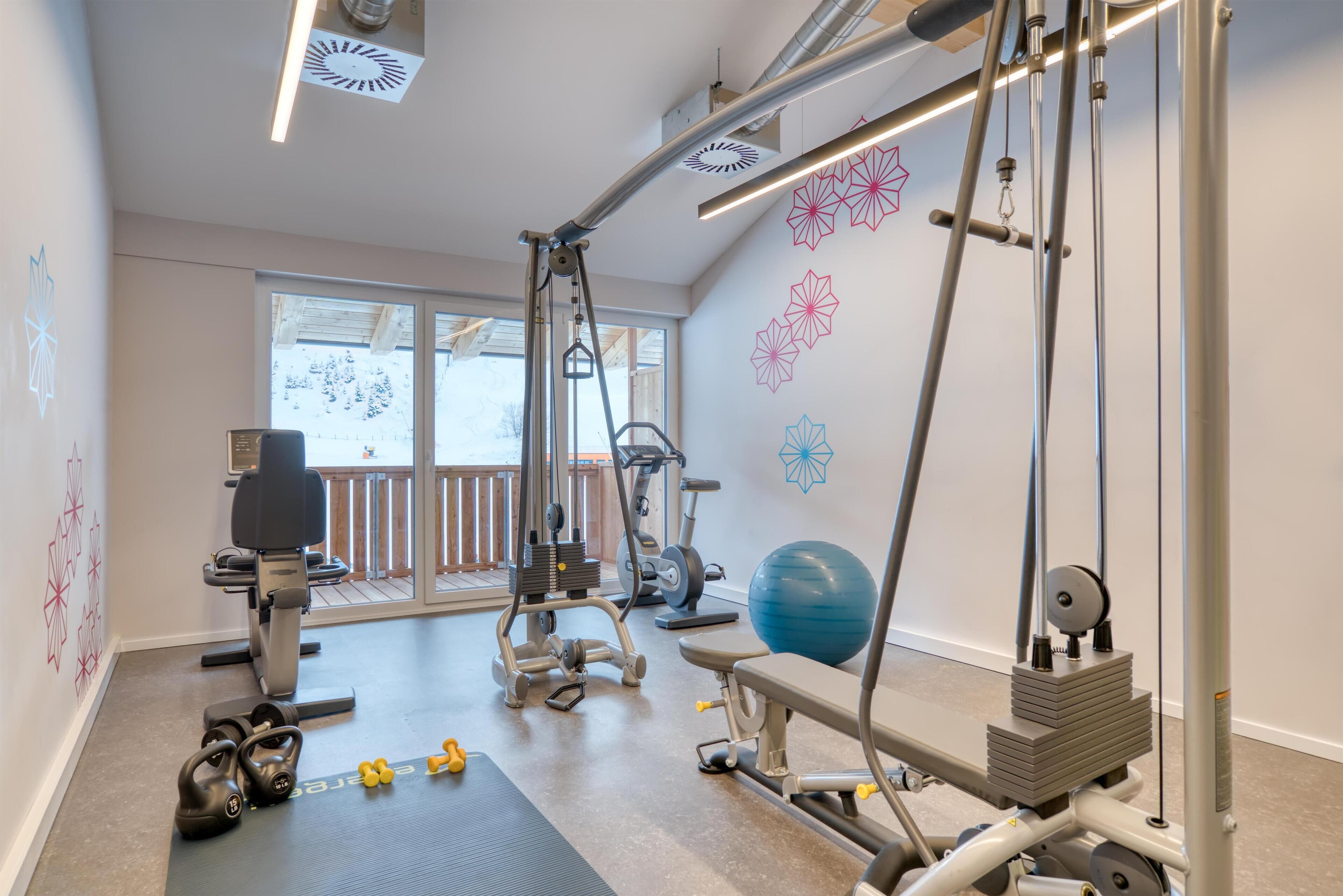 A gym with exercise equipment, a rowing machine, dumbbells, and a blue exercise ball.