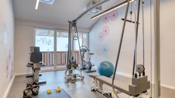 Une salle de sport équipée de matériel d’exercice, notamment un rameur, des haltères et un ballon d’exercice bleu.