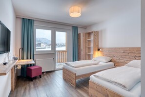 A modern hotel room with a wooden bed, a desk, and a view of snow-covered mountains. - COOEE alpin Hotel Bad Kleinkirchheim (Bad Kleinkirchheim)