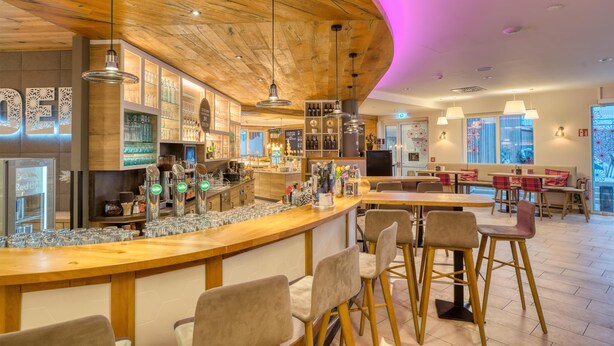 A modern bar area with wooden accents, a bar counter, and seating. - COOEE alpin Hotel Bad Kleinkirchheim (Bad Kleinkirchheim)