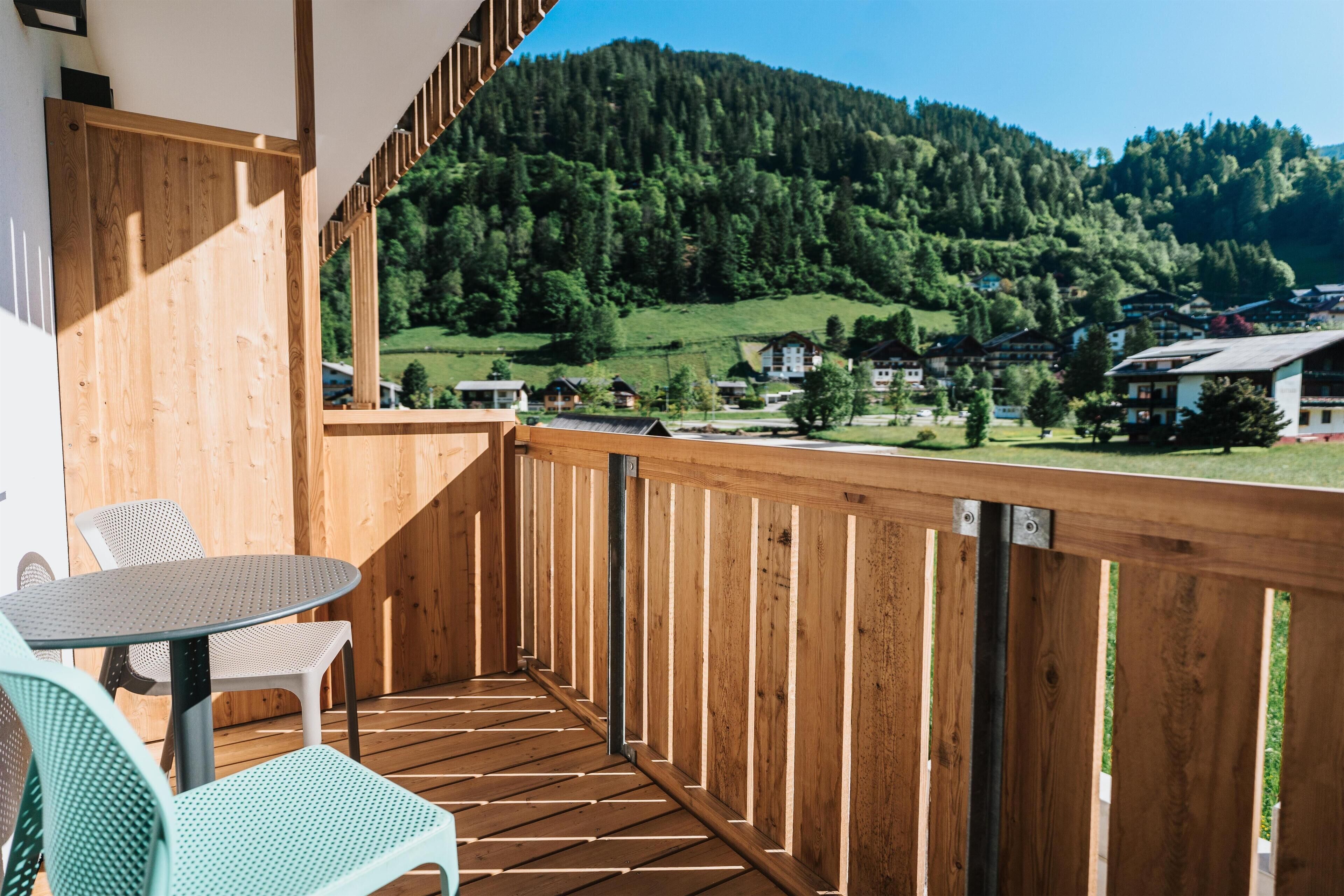 A wooden balcony with a table and chairs, overlooking a mountainous landscape with houses.