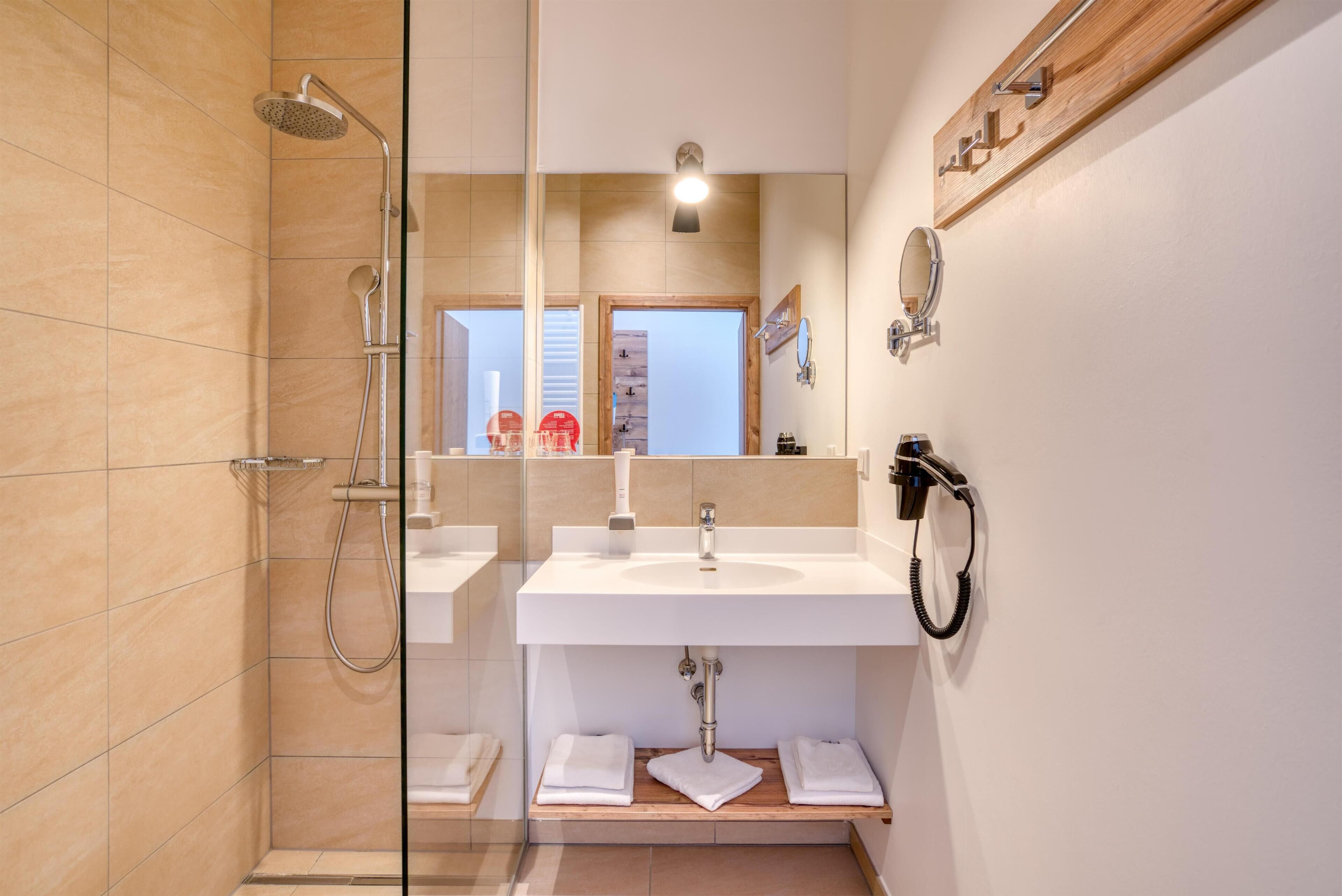 Un baño moderno con cabina de ducha de vidrio, un lavabo blanco y un espejo con repisa de madera encima.