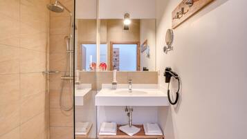 Un baño moderno con cabina de ducha de vidrio, un lavabo blanco y un espejo con repisa de madera encima.