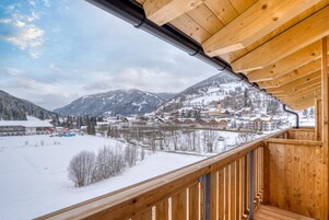 A wooden balcony with a view of a snow-covered village and mountains.