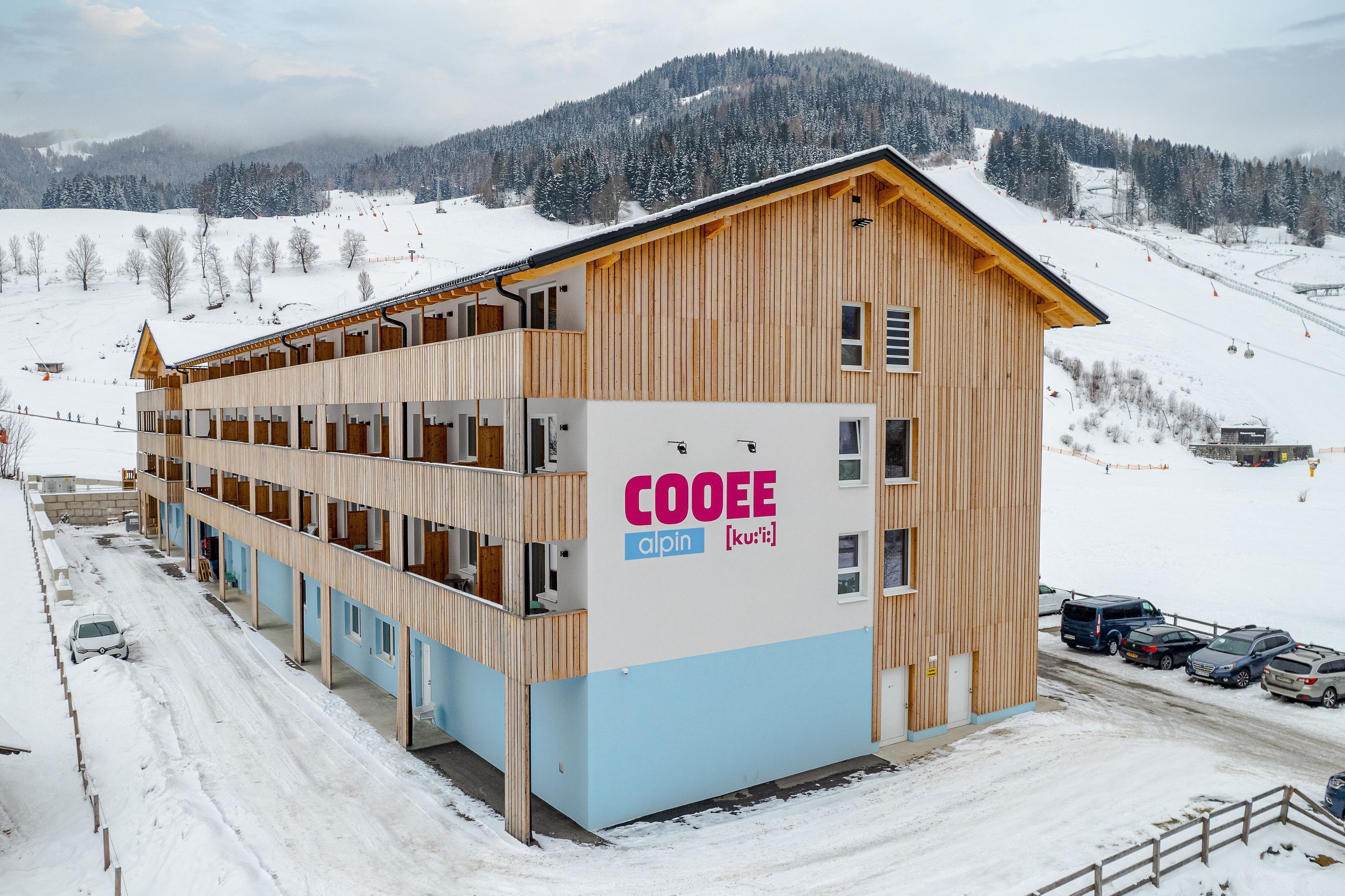 A multi-story wooden building with balconies, labeled 'COOEE alpin [ku-ri-t]'.