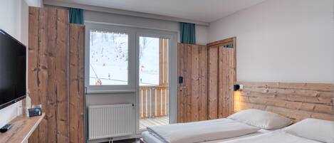 Un dormitorio con dos camas, un televisor, un armario de madera y vistas a un paisaje nevado.