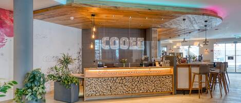 A modern reception area with a wooden ceiling, a counter with a stone pattern, and potted plants.