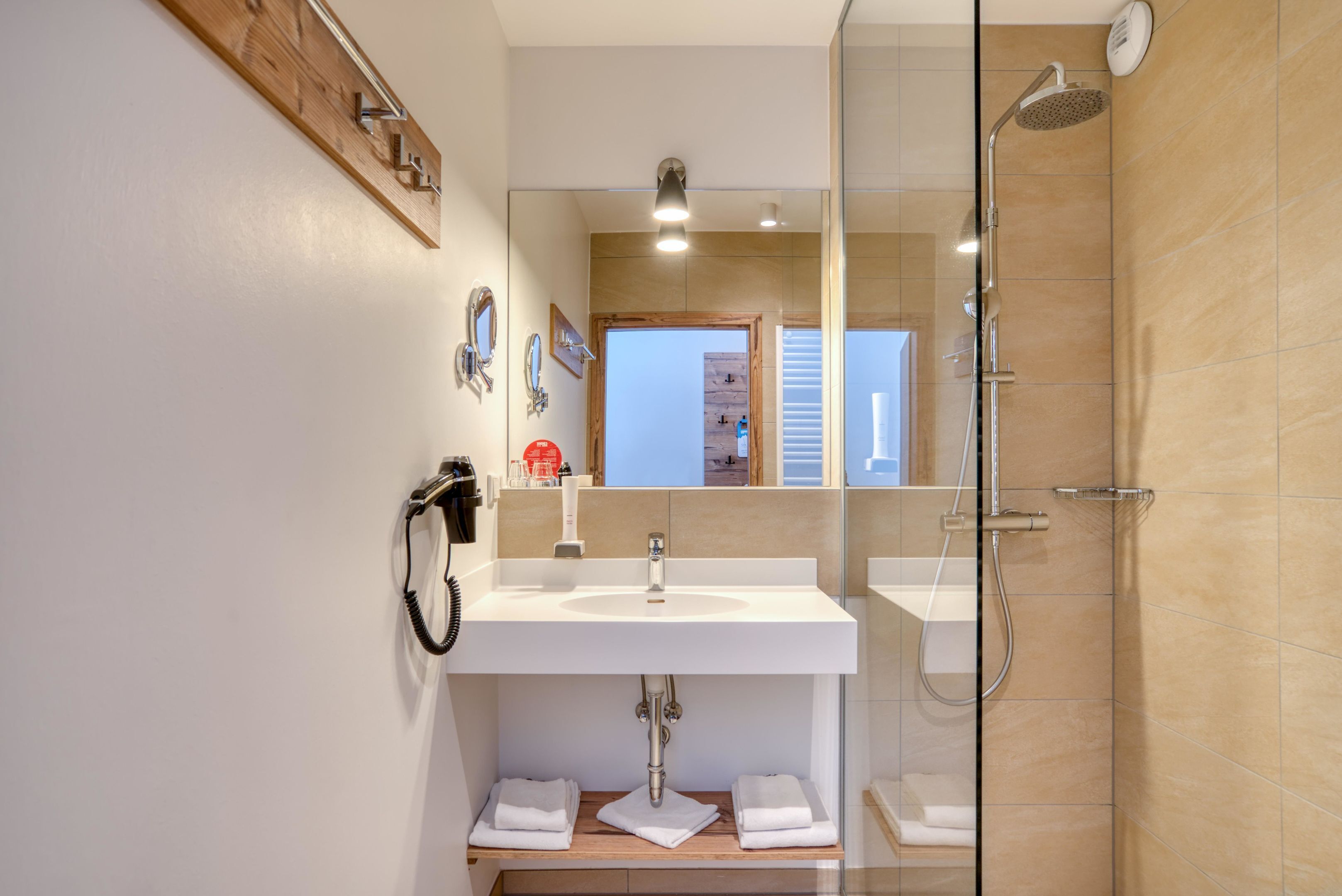 A modern bathroom with a sink, mirror, towel rack, and shower.