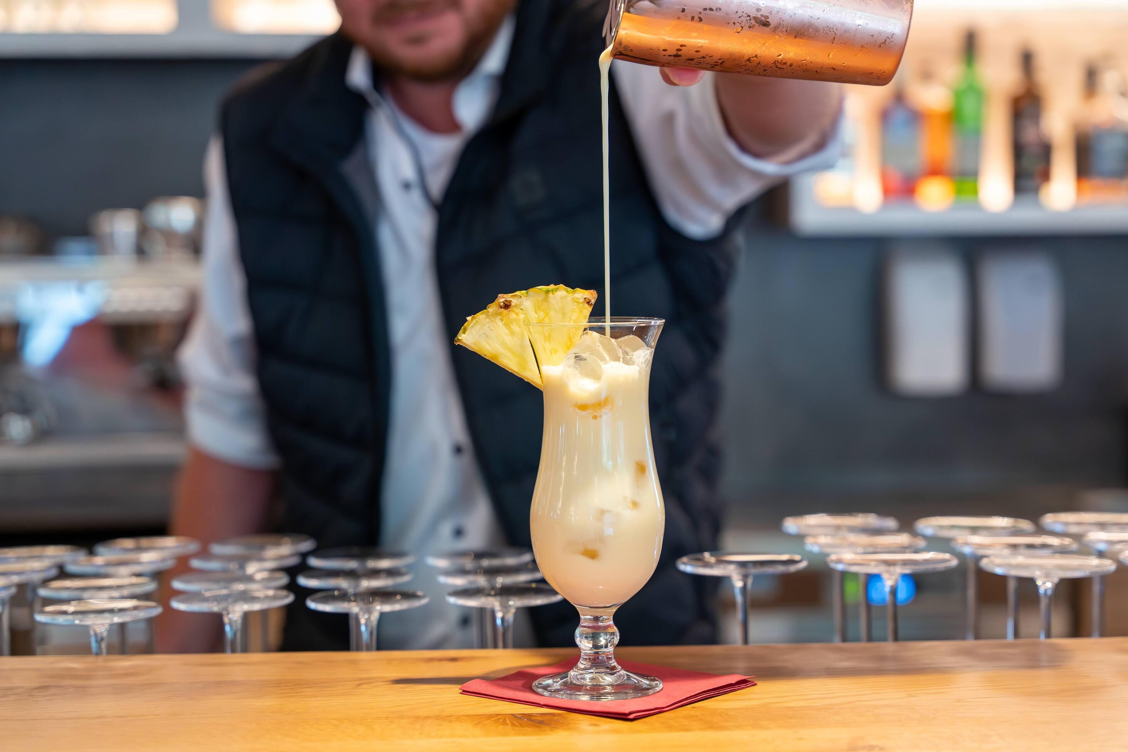 A bartender pouring a drink into a tall glass with a pineapple garnish.