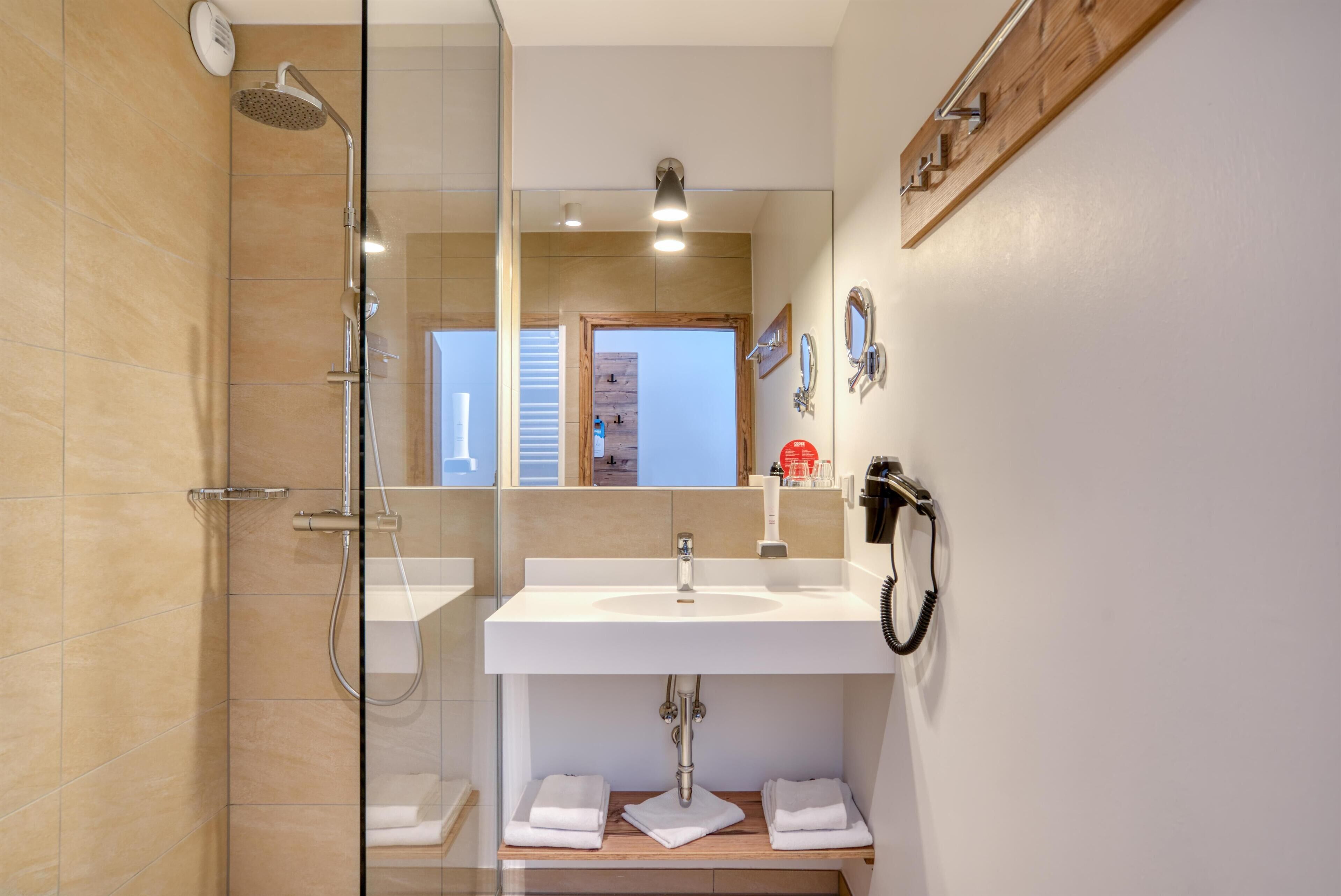 Un baño moderno con cabina de ducha de vidrio, un lavabo blanco y un mueble de tocador de madera.