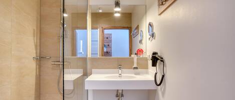 Un baño moderno con cabina de ducha de vidrio, un lavabo blanco y un mueble de tocador de madera.