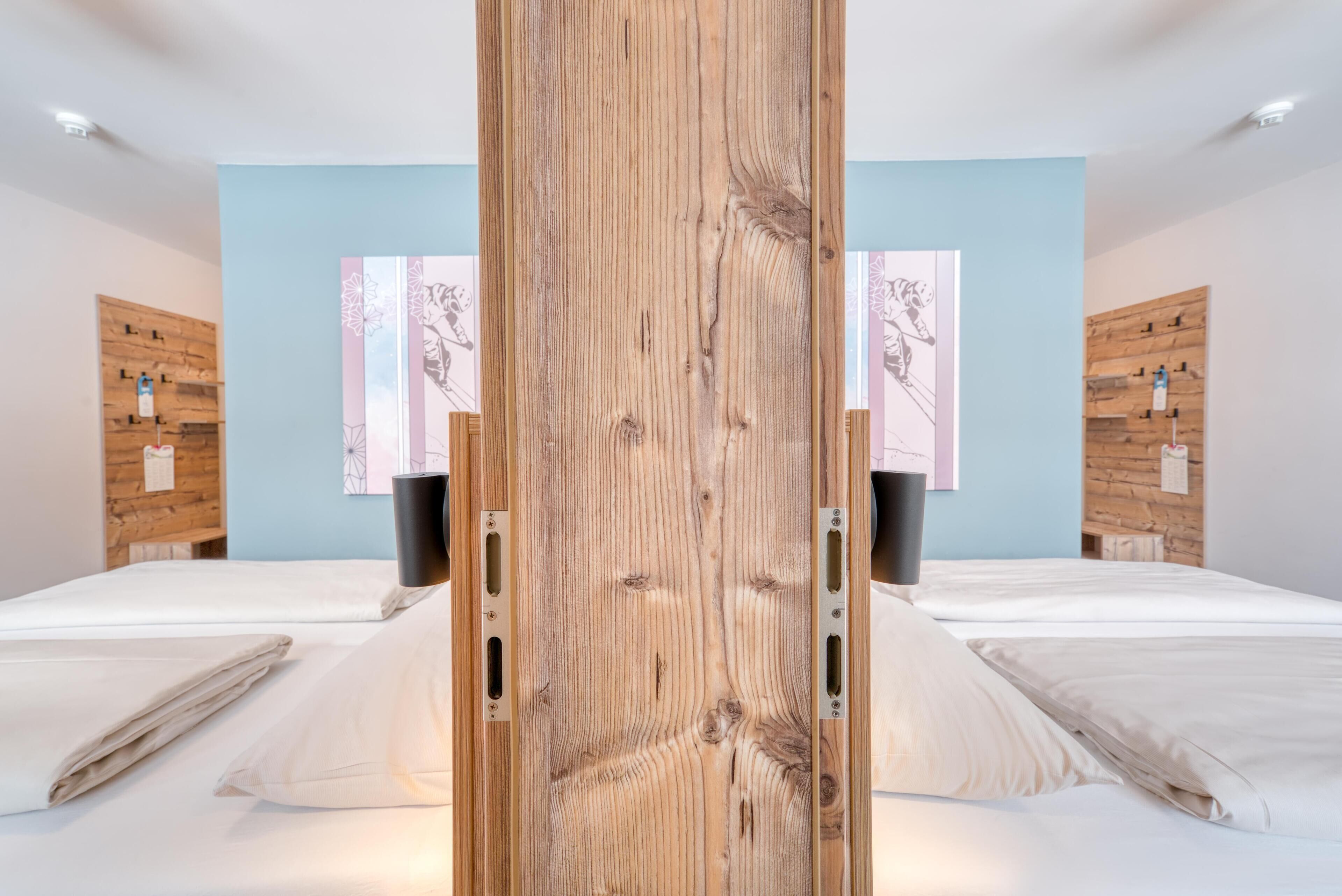 A modern hotel room with two beds, wooden headboards, and a light blue wall.