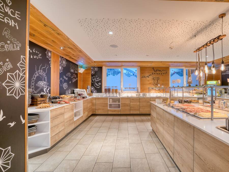 Un desayuno tipo buffet moderno con detalles de madera, una pared de pizarra con los artículos del menú y vistas al exterior.