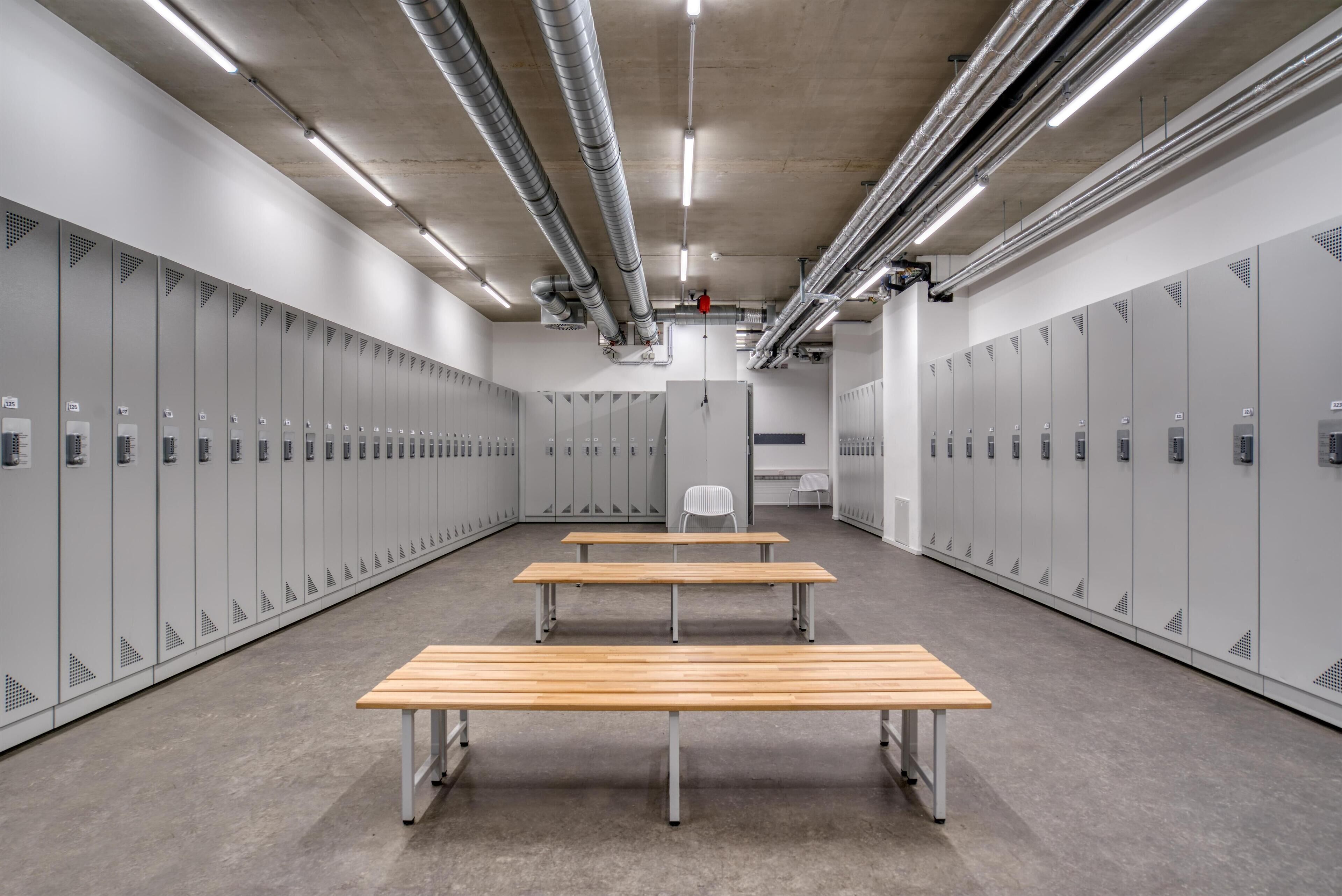 Un vestiaire équipé de plusieurs casiers, de deux bancs en bois et d’une chaise blanche.