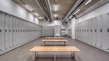 Un vestiaire équipé de plusieurs casiers, de deux bancs en bois et d’une chaise blanche.