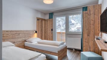 Ein Zimmer mit zwei Betten, Holzwänden, einem Fenster mit Blick auf schneebedeckte Gebäude und einem Schreibtisch mit Stuhl.