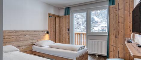 Une chambre avec deux lits, des murs en bois, une fenêtre donnant sur des bâtiments enneigés et un bureau avec une chaise.
