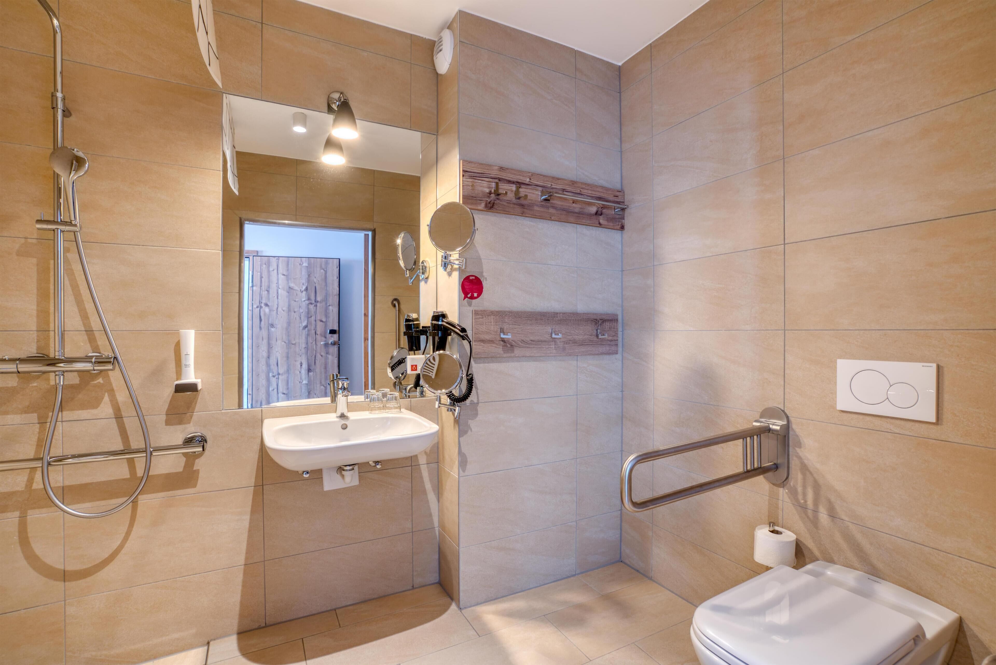 Een moderne badkamer met een wastafel, spiegel, douche en toilet.