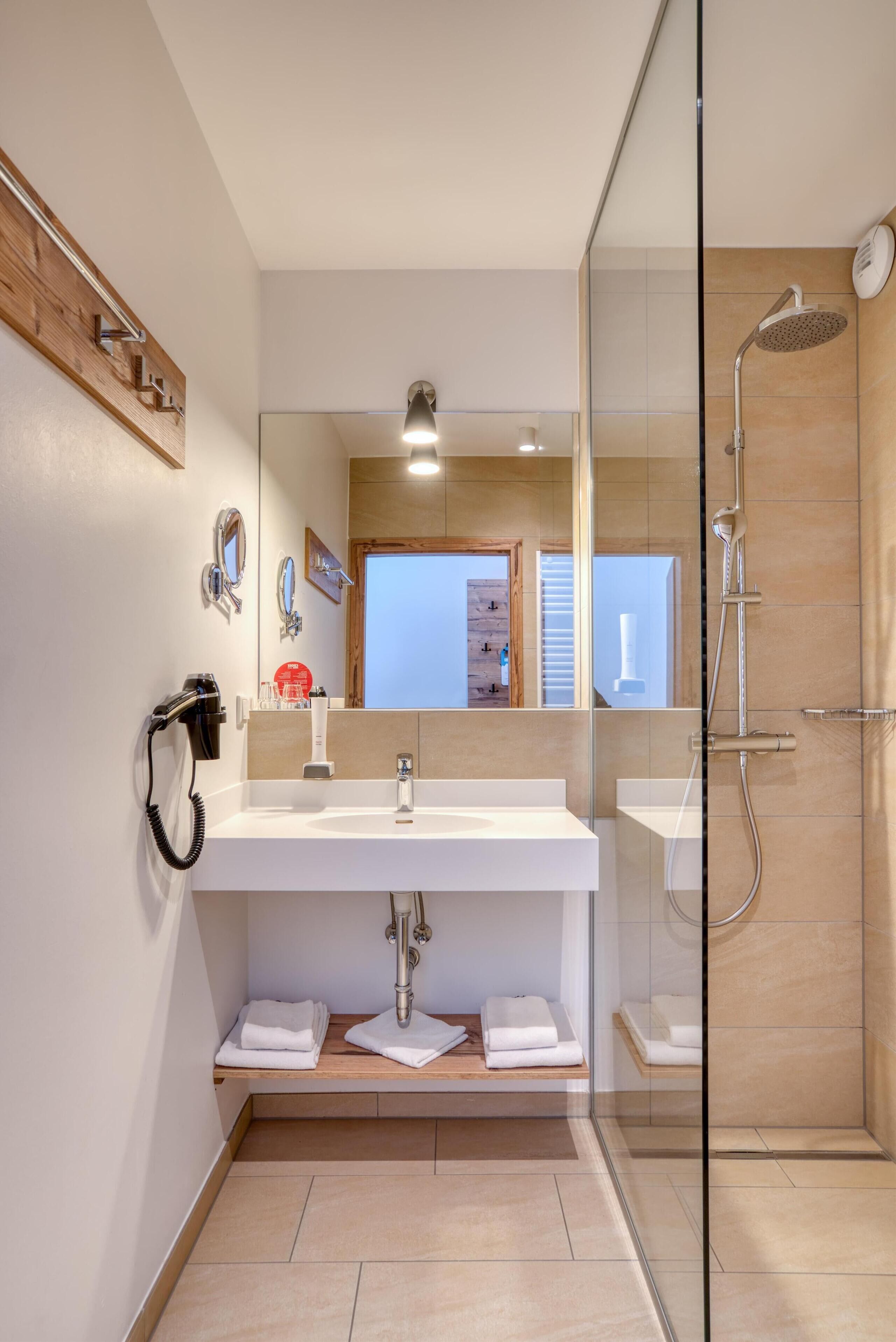 Une salle de bain moderne avec une douche à parois de verre, un grand miroir et un lavabo blanc.