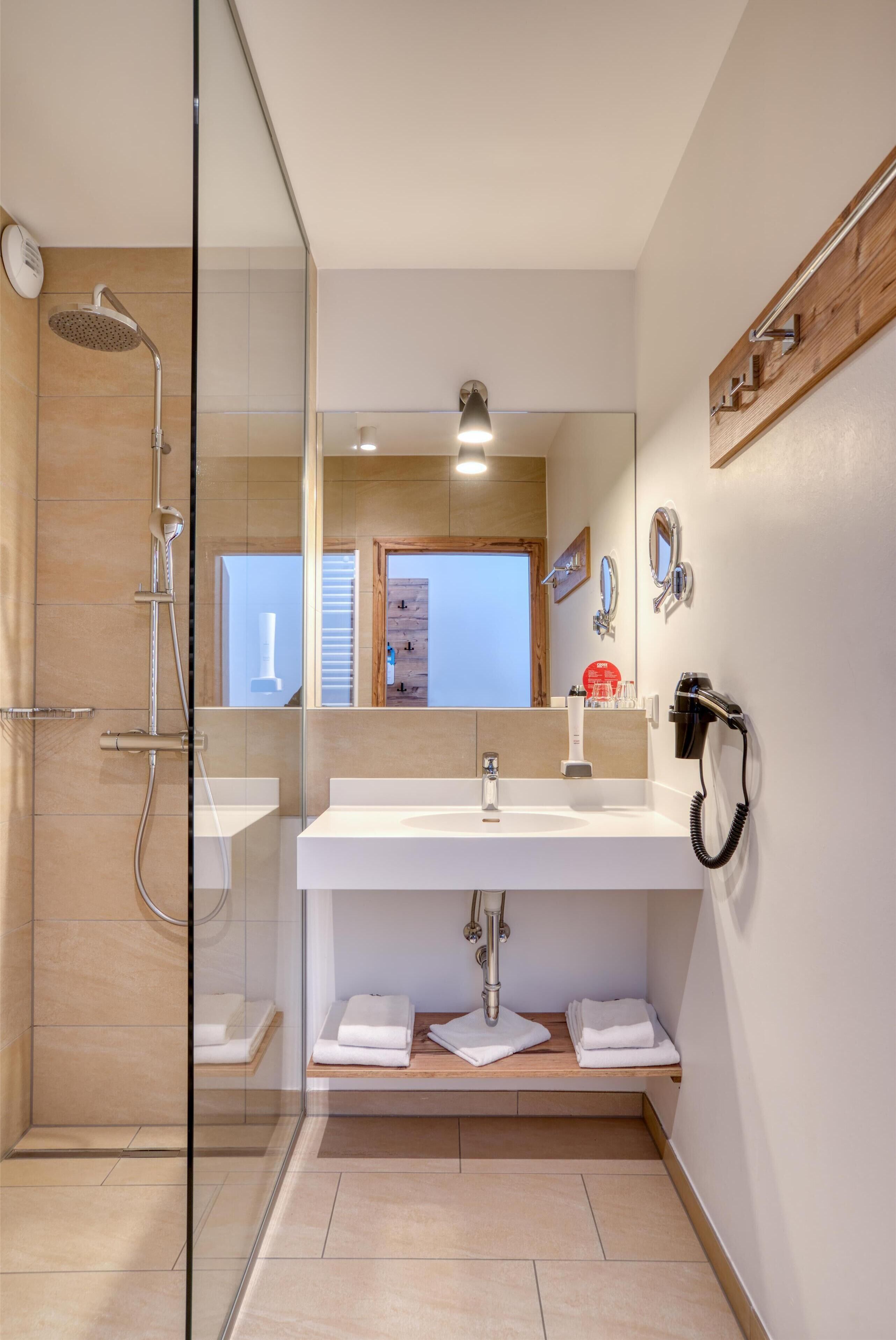 Ein modernes Badezimmer mit einer Duschkabine aus Glas, einem weißen Waschbecken und einem Spiegel.