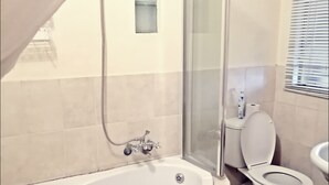 A bathroom with a bathtub, toilet, and shower area. - At Home Guesthouse (Upington)