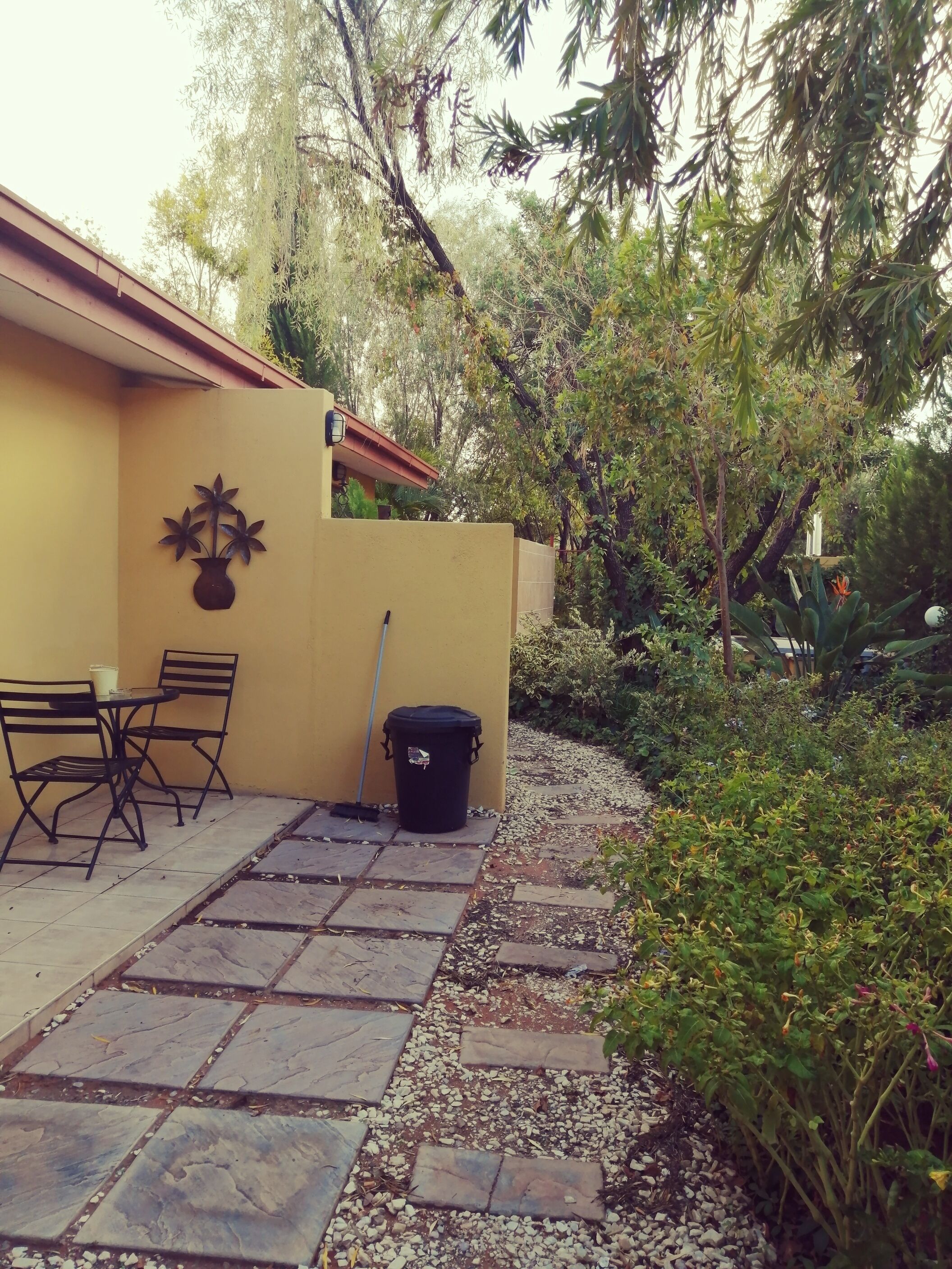 A patio area with a table and chairs, a trash bin, and a decorative wall piece.