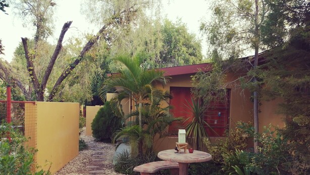 A garden pathway leading to a building with a red roof, surrounded by trees and plants. - At Home Guesthouse (Upington)