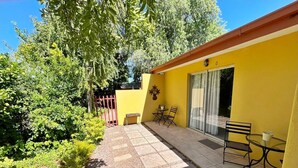 A yellow building with a patio area featuring a table and chairs, a small bench, and a gate. - At Home Guesthouse (Upington)
